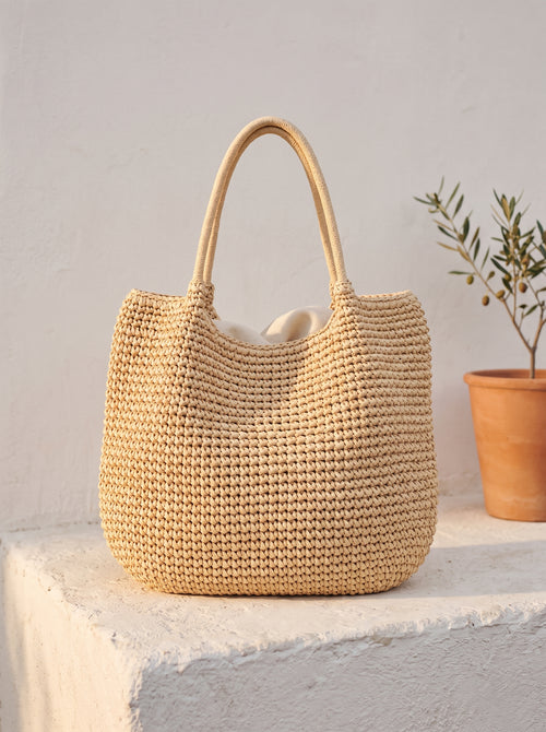 Bolso Duna de paja en beige, de pie sobre un poyete blanco
