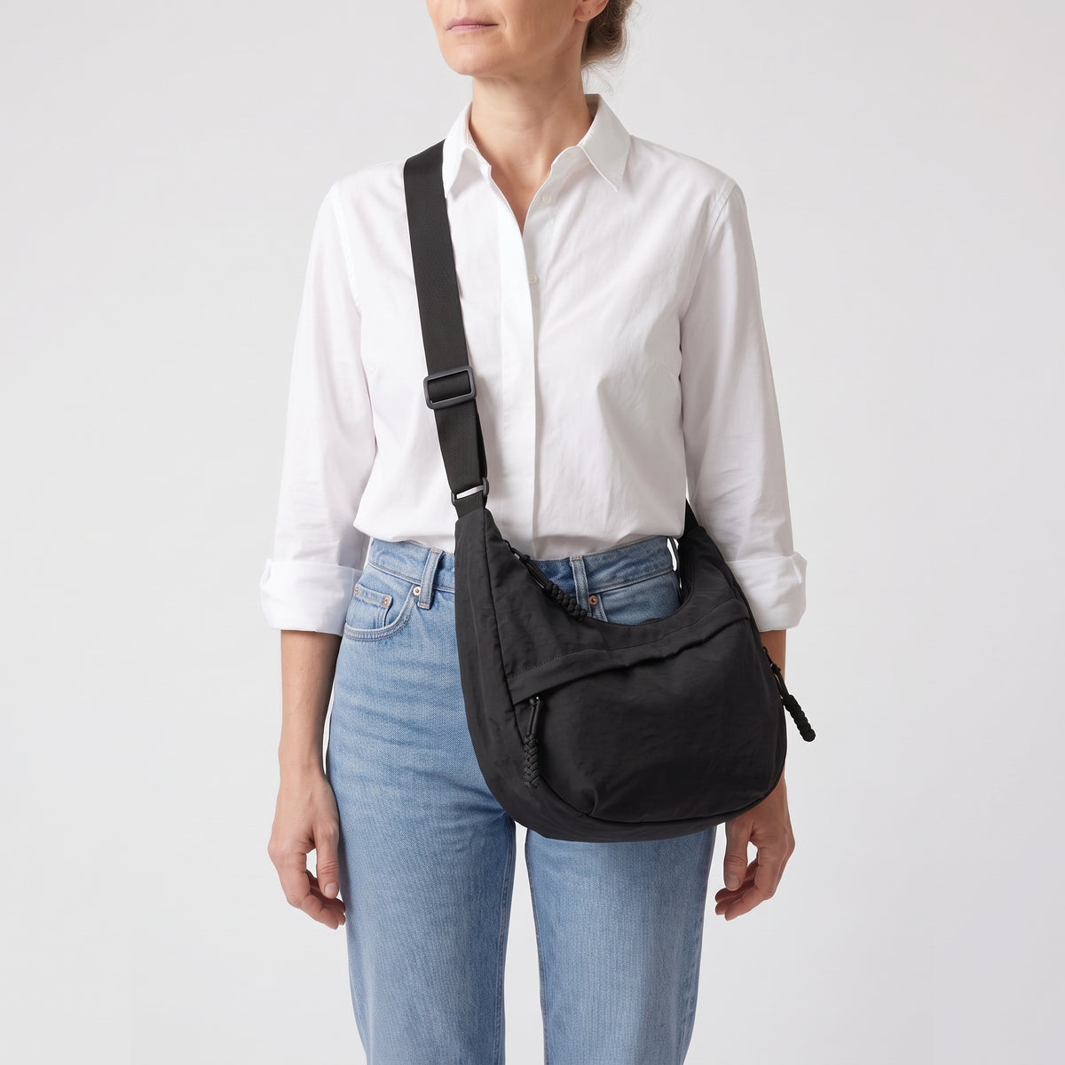 Mujer con camisa blanca lleva el bolso Nara negro cruzado por delante