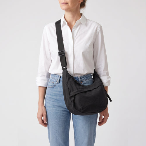 Mujer con camisa blanca lleva el bolso Nara negro cruzado por delante
